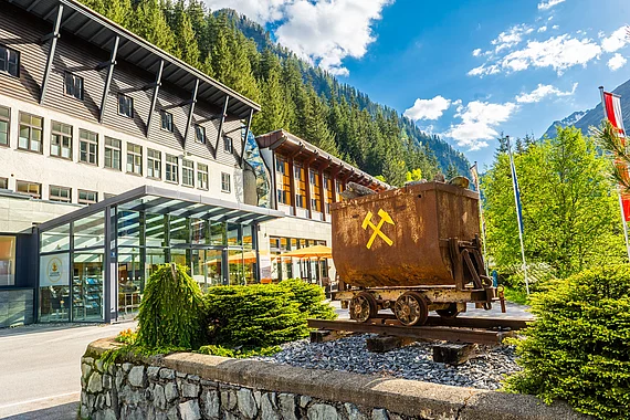 Außenansicht des Gesundheitszentrums Gasteiner Heilstollen mit Bergwerkswagen, der im Bergbau Grubenhunt genannt wird