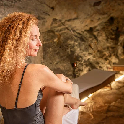 Seitliche Aufnahme einer Frau im Badeanzug mit geschlossenen Augen auf einer Liege im Heilstollen, umgeben von natürlicher Steinwand.