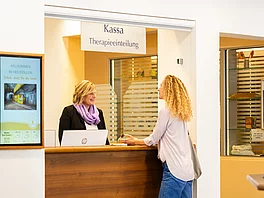 Frau wird von Mitarbeiterin empfangen und bekommt alle Informationen und wird für die Therapie eingeteilt