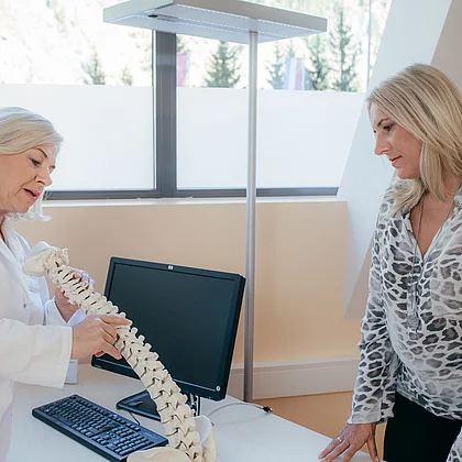 Patientin mit Fibromyalgie bei der Untersuchung, die Ärztin zeigt am Modell Wirbelsäule etwas vor im Gasteiner Heilstollen.