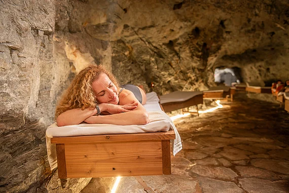 Frau entspannt in Badebekleidung auf einer Liege im Gasteiner Heilstollen – natürliche Schmerztherapie mit Radonwärme in einem Felsstollen.