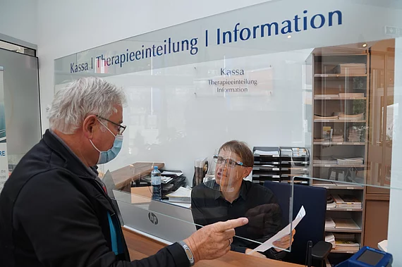 Patient mit Morbus Bechterew am Empfangsschalter bei der Anmeldung während Corona.
