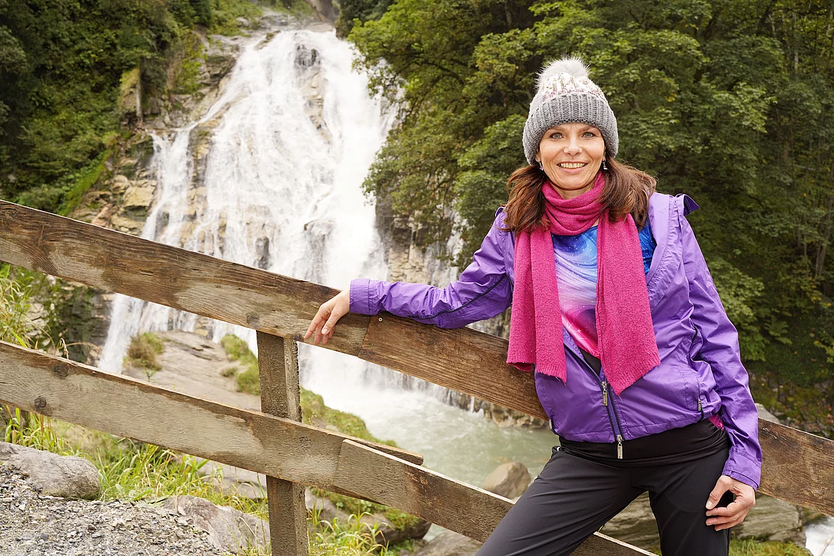 Patientin vom Gasteiner Heilstollen mit rheumatische Erkrankung und Morbus Bechterew steht vor Wasserfall.