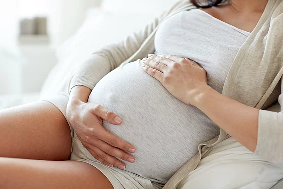 pregnancy, rest, people and expectation concept - close up of pregnant woman lying in bed and touching her belly at home