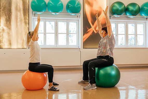 Patientin mit Morbus Bechterew trainiert mit Physiotherapeutin auf den Gymnastikbällen.