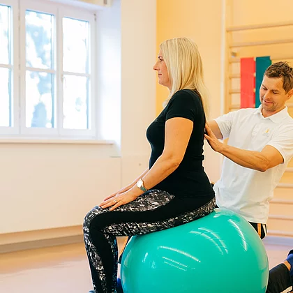 Patientin mit Fibromyalgie bei der Therapie auf dem Gymnastikball, der Therapeut richtet sie gerade im Gasteiner Heilstollen.