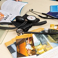 Person notiert sich etwas und daneben liegen einige Prospekte und ein Steskop vom Heilstollen.