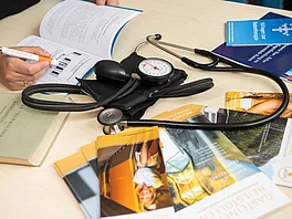 Person notiert sich etwas und daneben liegen einige Prospekte und ein Steskop vom Heilstollen.