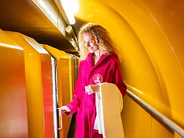 Die Patientin steht im Bademantel vorm Waggon des Heilstollen-Zugs und sieht in das Abteil