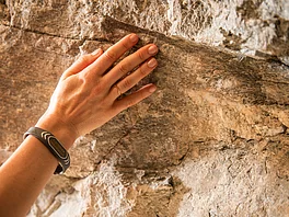 Hand einer Patientin berührt das Gestein des Gasteine Heilstollen während der Radontherapie