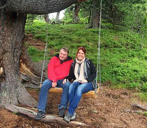 Frau und Mann sitzen auf einer Schaukel im Wald.