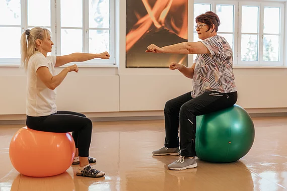 Patientin mit Morbus Bechterew trainiert mit Physiotherapeutin auf den Gymnastikbällen.