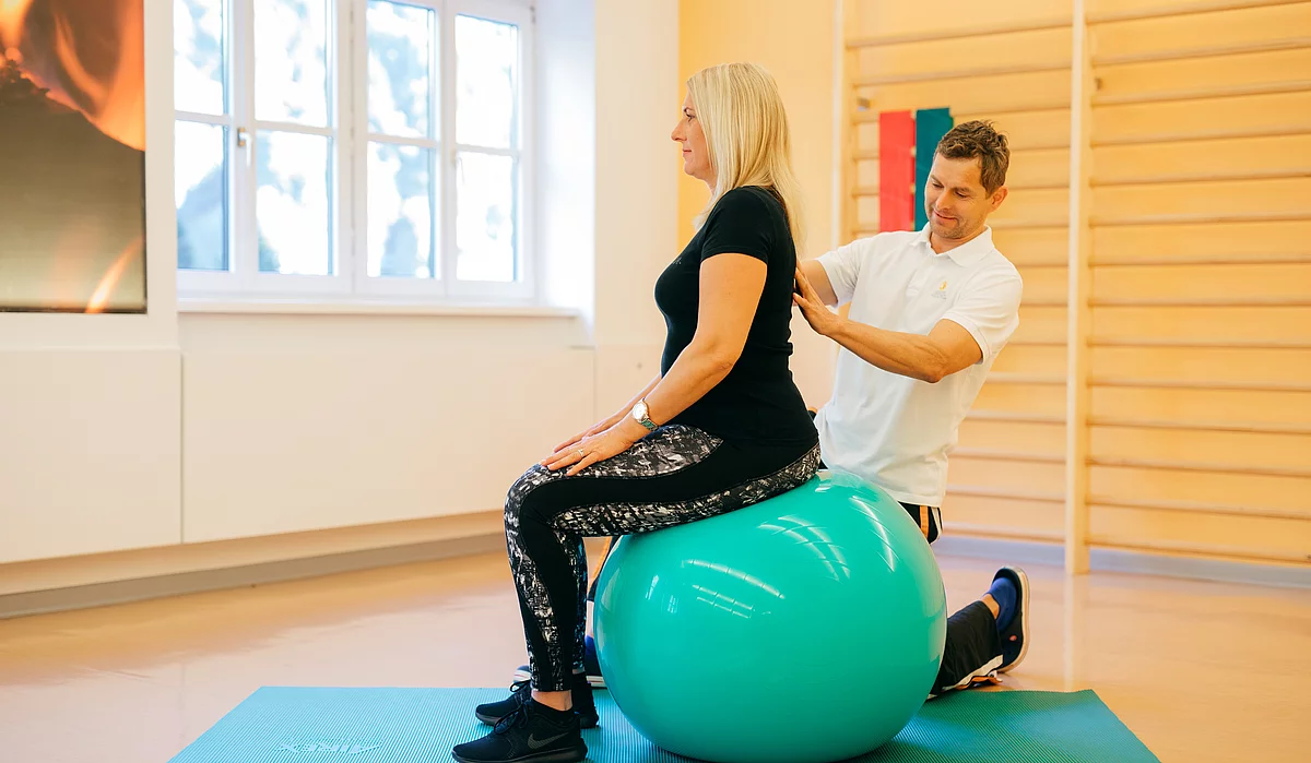 Patientin mit Fibromyalgie bei der Therapie auf dem Gymnastikball, der Therapeut richtet sie gerade im Gasteiner Heilstollen.