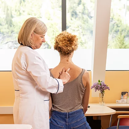 Ärztin tastetn manuell den Rücken/die Wirbelsäule der Patientin ab