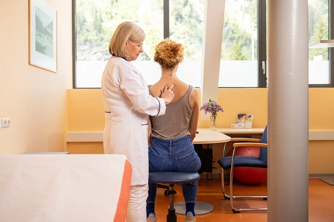 Ärztin tastetn manuell den Rücken/die Wirbelsäule der Patientin ab